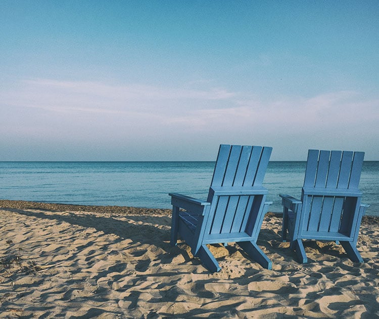 Empty beach chairs on sand facing the ocean.