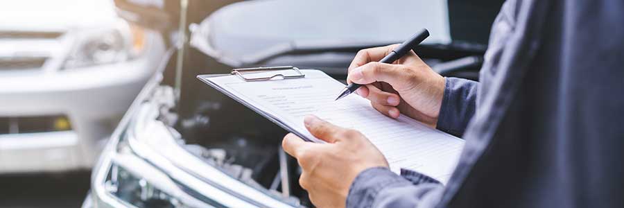 A mechanic with a clipboard under the hood of a car.