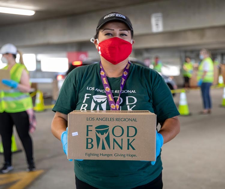 Woman in a red face mask holding a food bank box at a warehouse