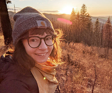 Young woman in a beanie on a mountain at sunset