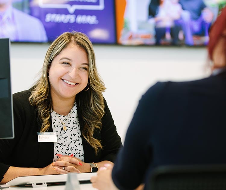 A SchoolsFirst FCU teammember helping a Member at a desk.